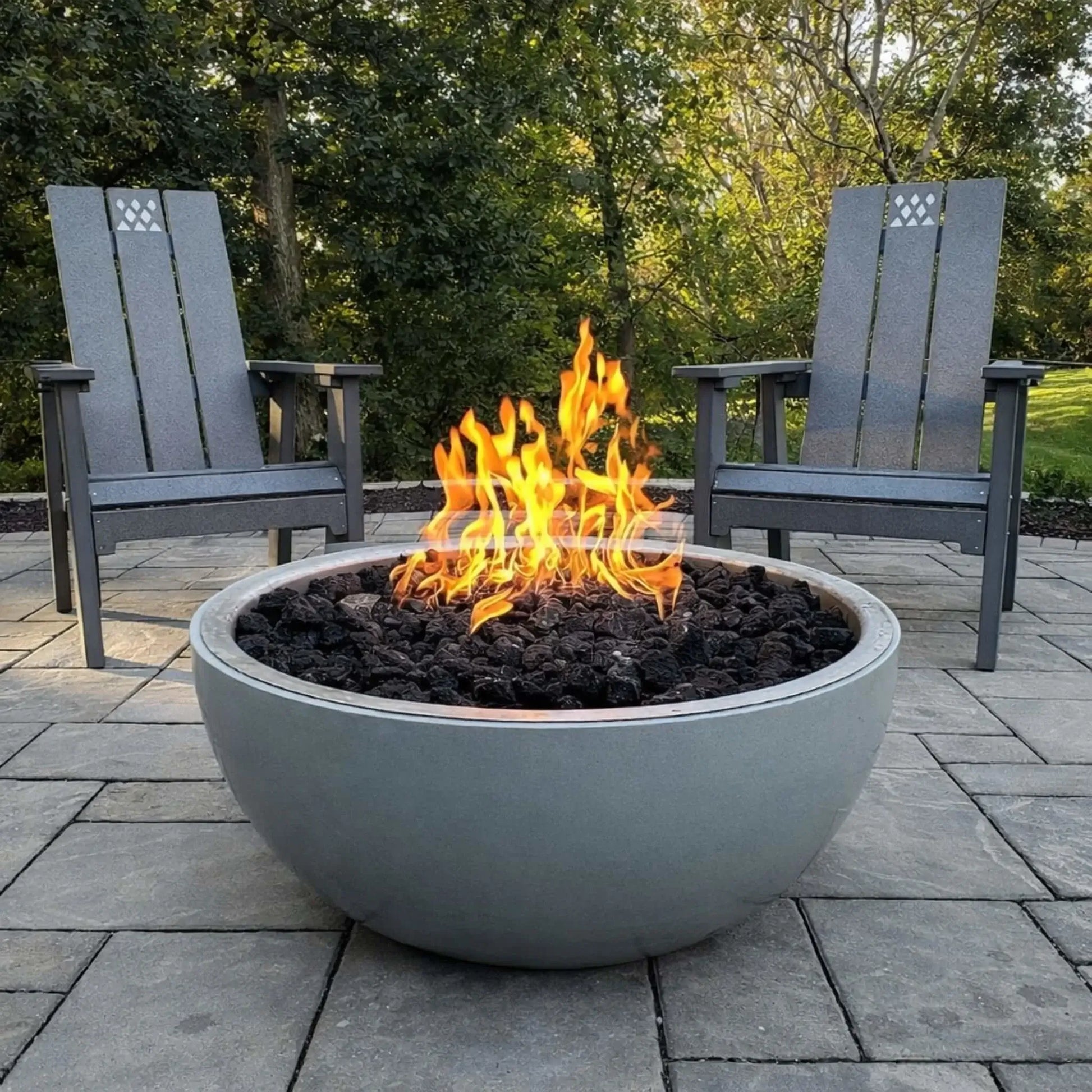 HPC Fire Inspired Hearth Products concrete penta torpedo fire bowl installed on a patio, filled with black lava rock and active flames, surrounded by outdoor Adirondack chairs, creating a warm and inviting backyard fire pit setting.