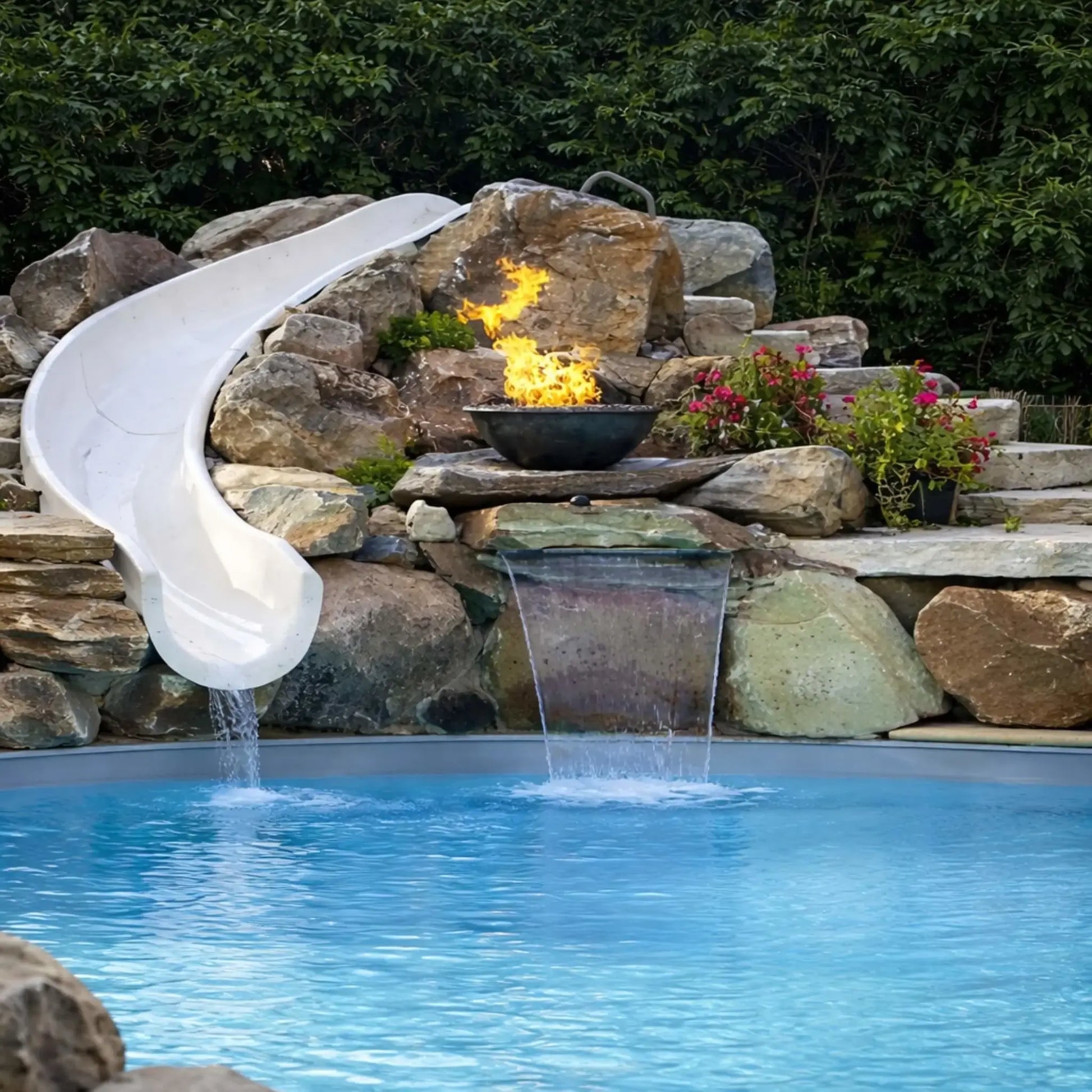 Centered view of a custom pool waterfall installation with HPC Tempe Series copper fire bowl mounted on stacked stone. A white slide flows into the pool on the left, while dual water streams spill below the fire feature. The combination of fire, water, and natural rock creates a balanced, high-end backyard design.