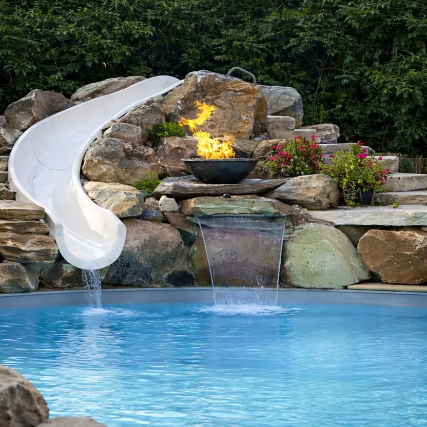 Centered view of a custom pool waterfall installation with HPC Tempe Series copper fire bowl mounted on stacked stone. A white slide flows into the pool on the left, while dual water streams spill below the fire feature. The combination of fire, water, and natural rock creates a balanced, high-end backyard design.