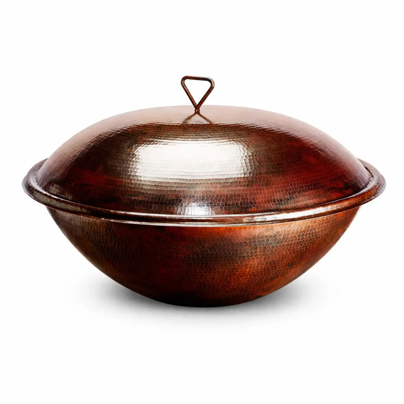 Installed hammered copper burner cover on a Tempe fire bowl, featuring a rounded dome lid with a triangular handle and a deep bowl base. The copper’s natural patina and textured surface reflect light beautifully, while the clean white background keeps focus on the elegant shape and durable outdoor design.