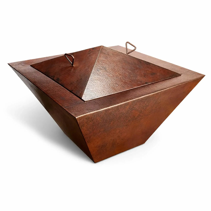 Large 40-inch Sedona square fire pit burner cover installed on a matching bowl, featuring a pyramid-style lid with dual handles and a wide square base. The hammered copper texture and natural patina add depth and character, while the white background enhances the bold geometric design and premium finish.