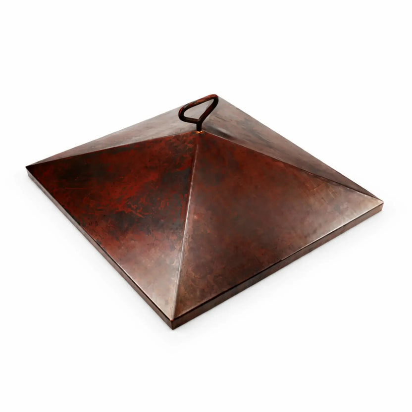 36-inch Sierra square burner cover featuring a sleek pyramid-shaped copper lid with a single loop handle. The smooth, slightly weathered copper surface shows natural patina variations, giving it a rustic yet refined look. Set against a white background to clearly display the geometric design and durable construction.