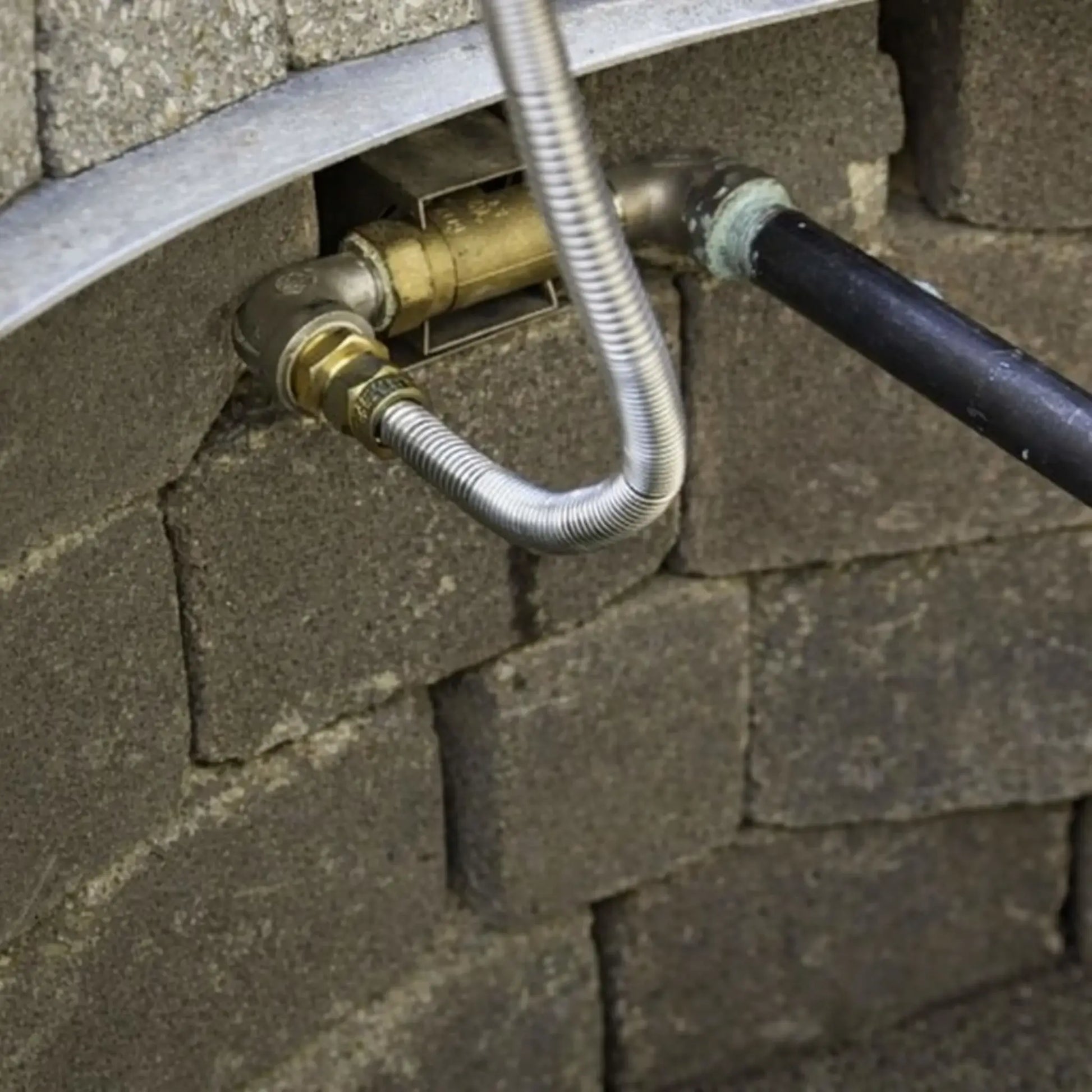 Installed straight key valve inside a masonry fire pit wall, showing brass valve body connected to gas piping and flexible stainless steel line, demonstrating real-world fire pit gas control setup within stone block construction.