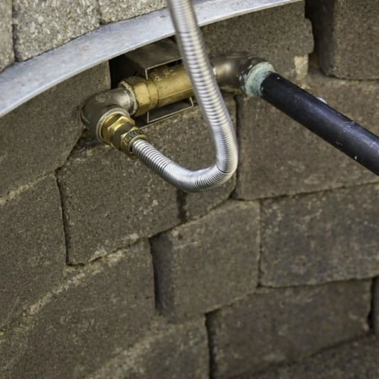 Installed straight key valve inside a masonry fire pit wall, showing brass valve body connected to gas piping and flexible stainless steel line, demonstrating real-world fire pit gas control setup within stone block construction.