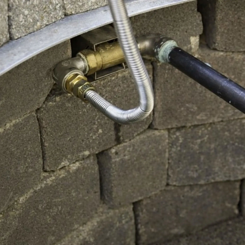 Installed straight key valve inside a masonry fire pit wall, showing brass valve body connected to gas piping and flexible stainless steel line, demonstrating real-world fire pit gas control setup within stone block construction.