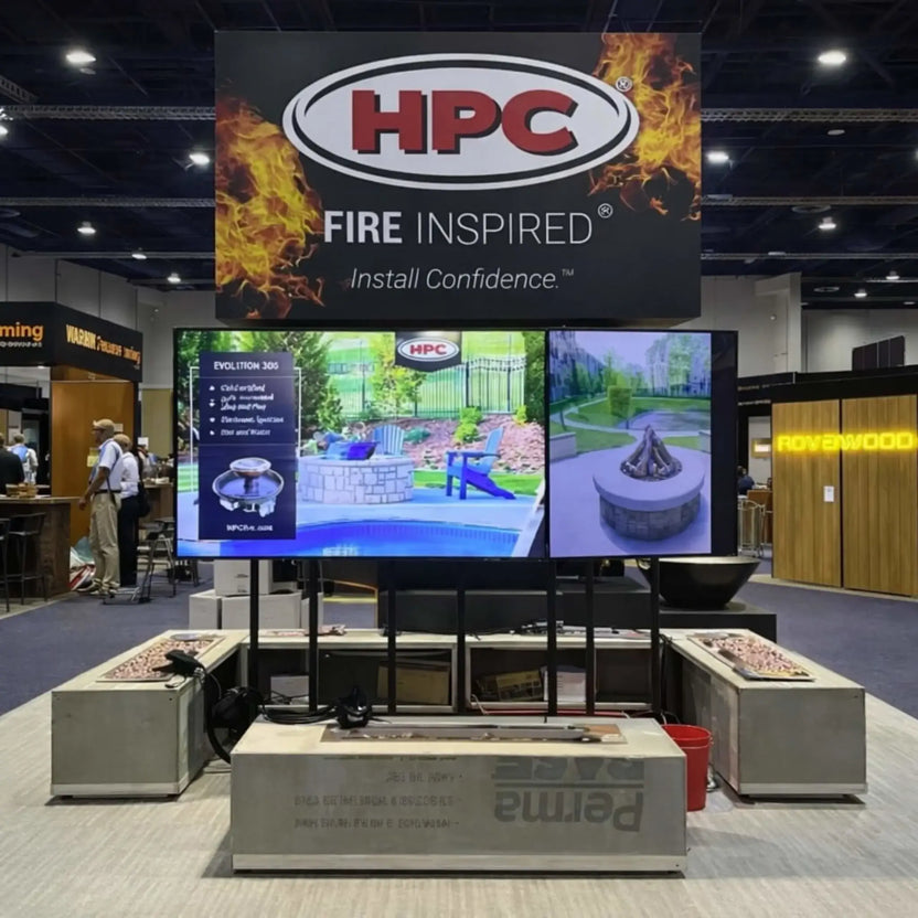 Trade show display featuring HPC Fire Inspired branding above multiple fire pit table units. The setup includes demonstration screens, linear fire pit enclosures, and product showcases, emphasizing professional-grade outdoor fire feature solutions.