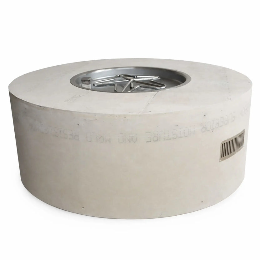 Studio product image of a round ready-to-finish fire pit table enclosure made from cement board, featuring a recessed stainless steel burner pan with a star-shaped burner. The cylindrical structure includes a smooth unfinished exterior and a built-in side vent, designed for custom finishing in outdoor patio or backyard fire feature installations.