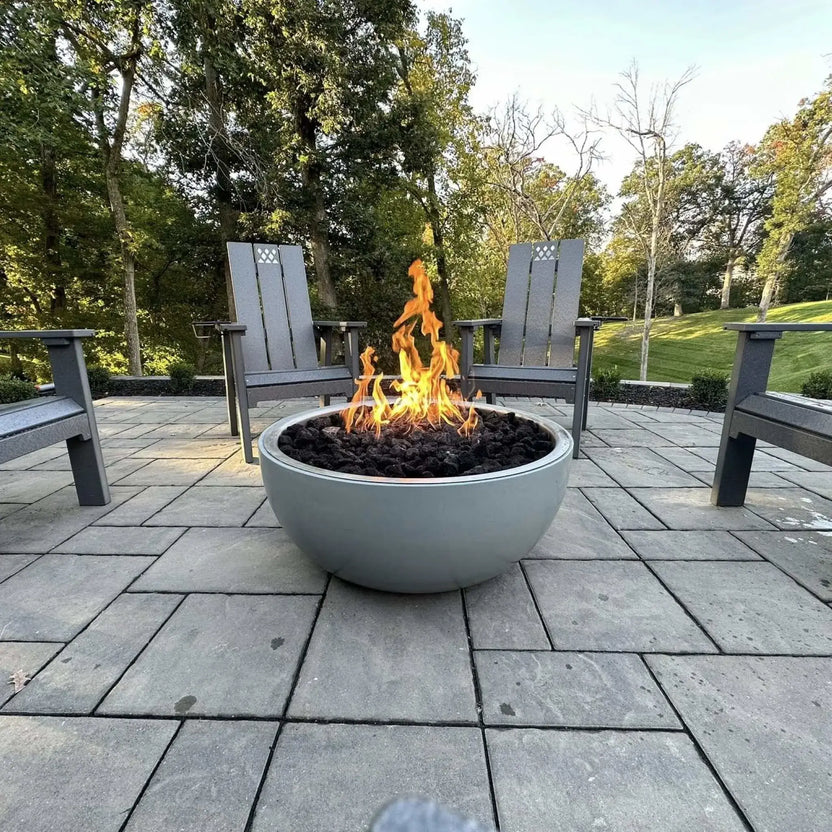 HPC Fire Inspired Hearth Products FPPK push button flame sensing penta burner featured in a modern round concrete fire bowl on a paver patio. Flames rise through dark lava rock, framed by Adirondack-style chairs and a tree-lined backyard, emphasizing a balanced, evenly distributed flame pattern.