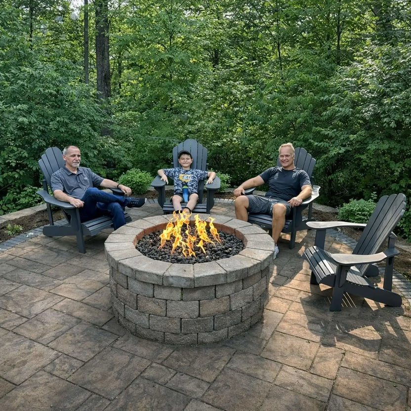 HPC Fire Inspired Hearth Products round flat FPPK push button flame sensing standard torpedo penta burner highlighted in a backyard patio scene with three people relaxing in Adirondack chairs around a circular fire pit. The fire glows over dark lava rock, emphasizing social outdoor living and comfortable seating arrangements.