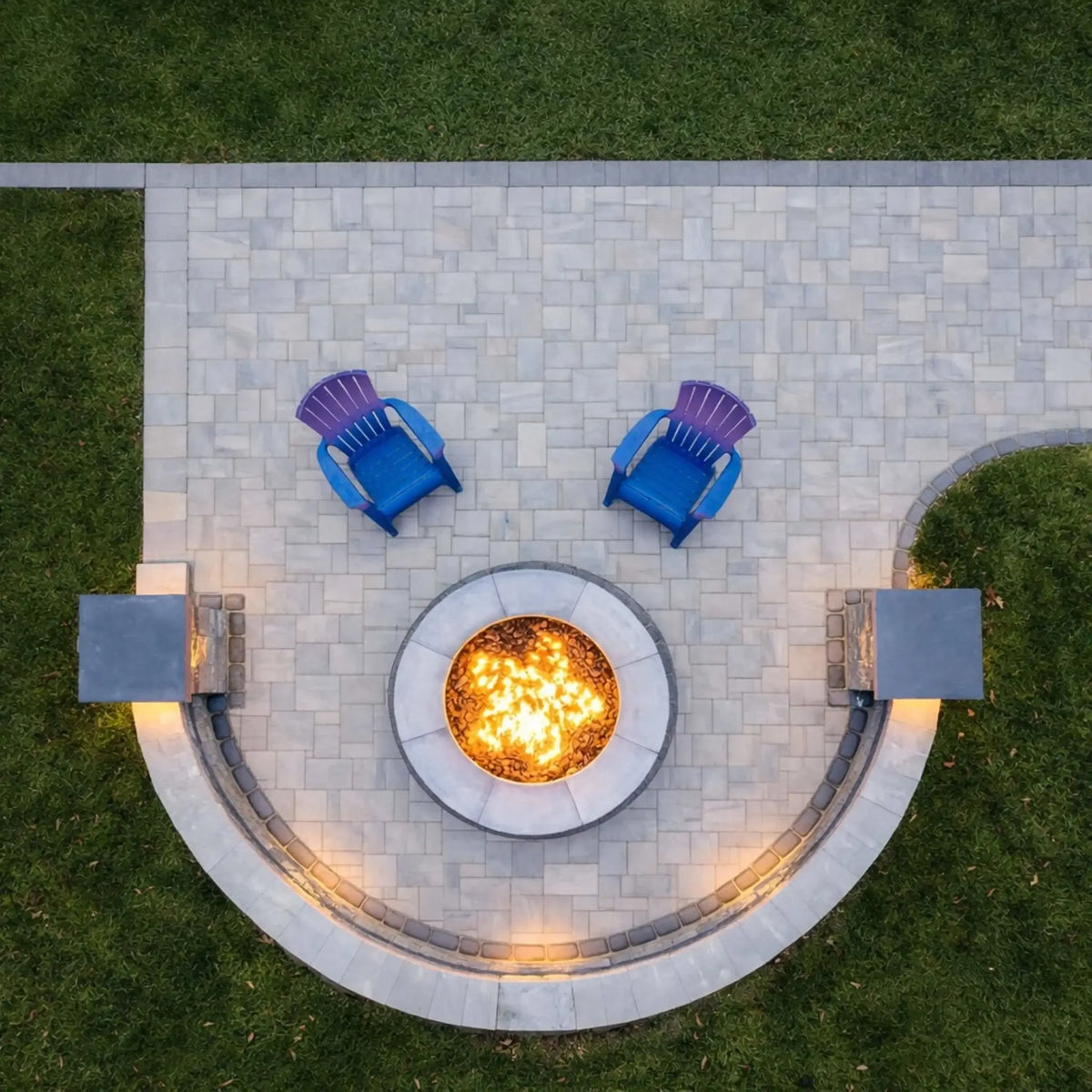HPC Fire Inspired Hearth Products round flat match lit CSA MLFPK FLEX standard torpedo penta burner featured in an overhead view of a circular patio fire pit. The glowing flame sits at the center of a symmetrical stone layout with two blue Adirondack chairs, highlighting a balanced outdoor seating arrangement ideal for social gatherings.