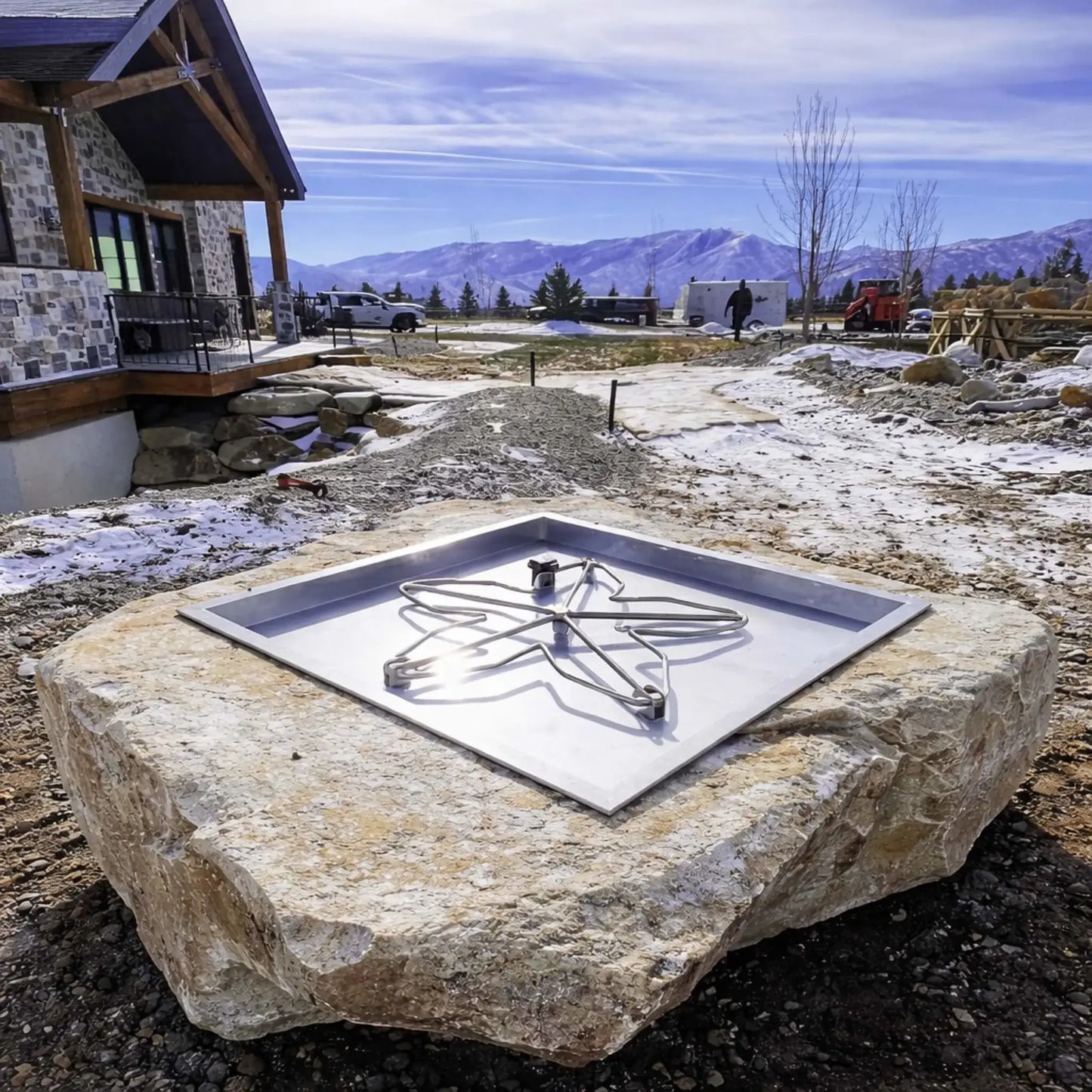 HPC Fire Inspired Hearth Products torpedo penta burner installed into a natural stone slab fire pit in a mountain setting, shown unlit to emphasize the square drop-in pan and burner structure. Snow-dusted ground and scenic landscape highlight a rugged, high-end outdoor installation environment.