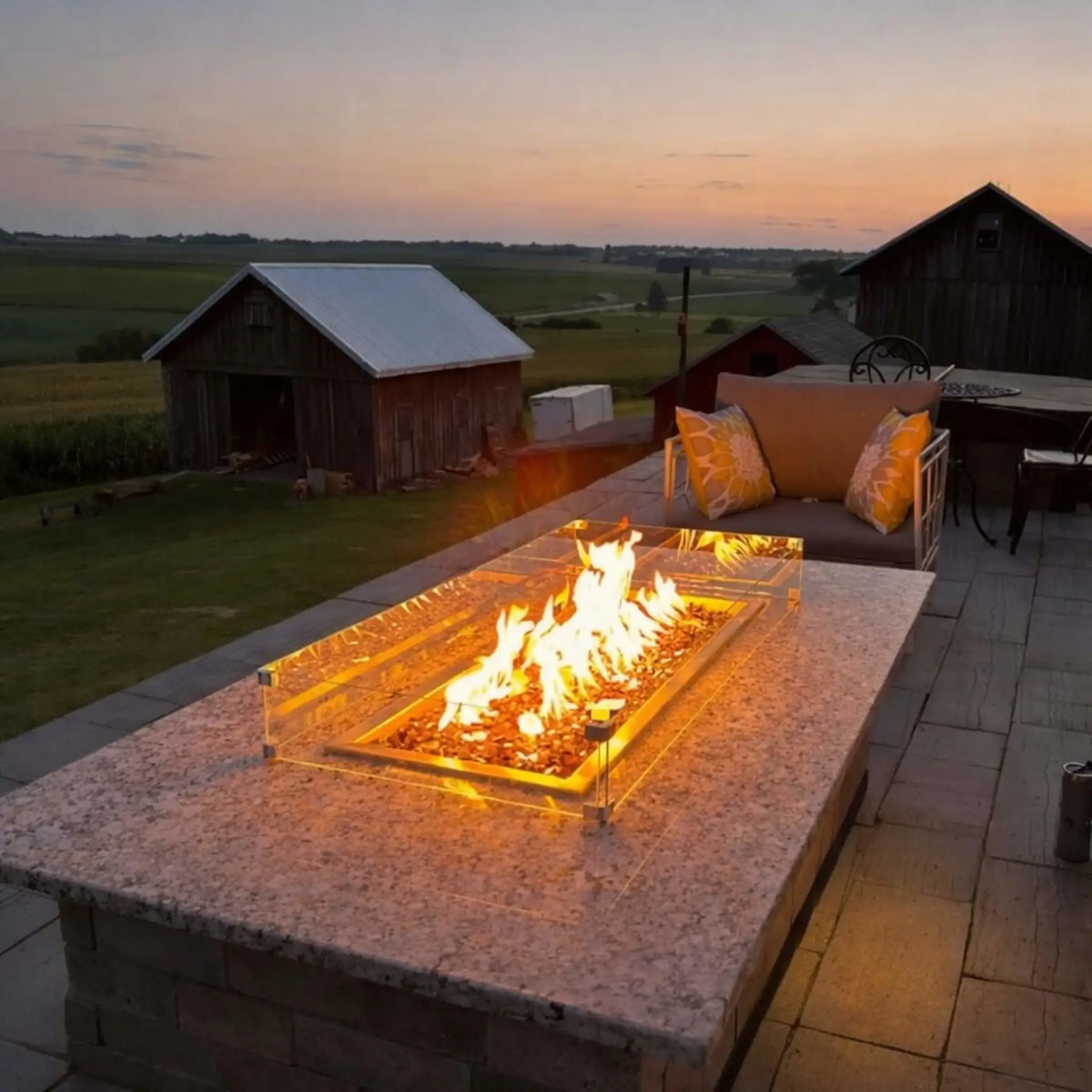 Hearth Products Controls HPC Fire rectangle drop in pan H burner torpedo electronic ignition Hi Lo low lifestyle setup on a rooftop patio at sunset, featuring a granite fire table with glass wind guard and bright flames, easily controlled by remote or mobile app with adjustable high and low flame settings for outdoor ambiance.