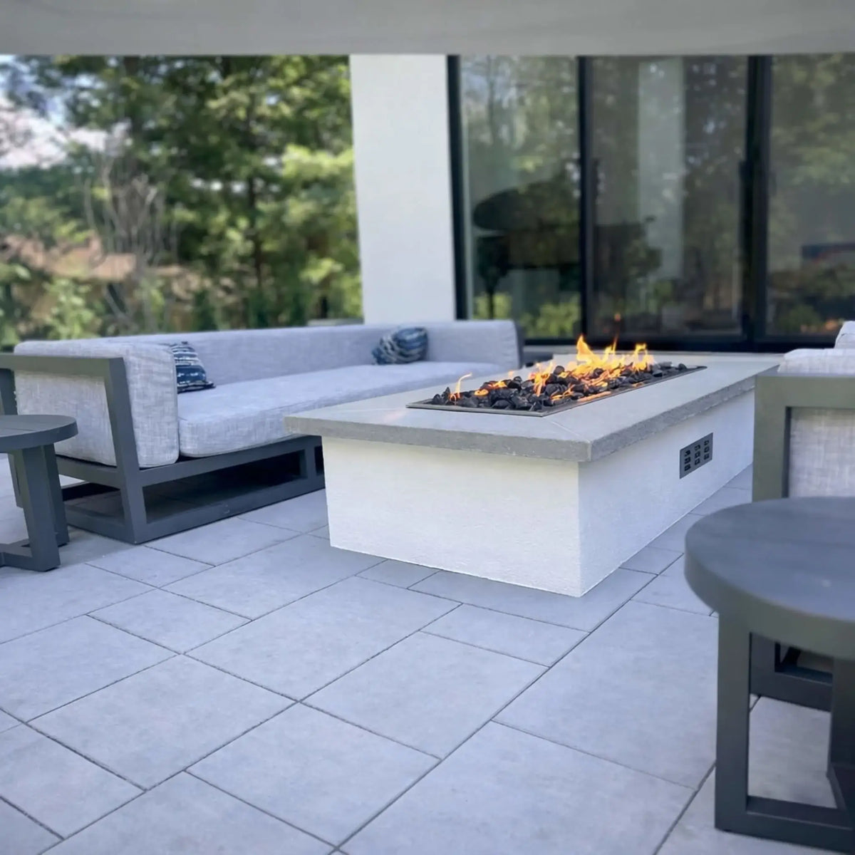 Hearth Products Controls HPC Fire rectangle drop in pan H burner torpedo electronic ignition Hi Lo low modern outdoor living space with white fire table and cushioned seating, featuring a sleek linear flame design controlled via remote or smartphone app with adjustable high and low heat output.