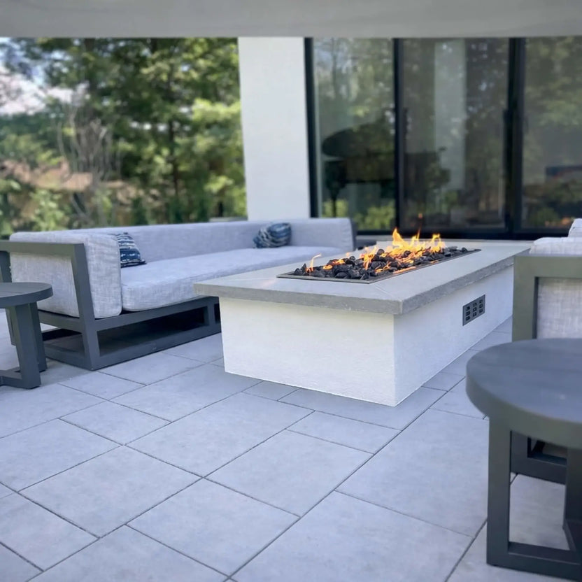 Hearth Products Controls HPC Fire rectangle drop in pan H burner torpedo electronic ignition Hi Lo low modern outdoor living space with white fire table and cushioned seating, featuring a sleek linear flame design controlled via remote or smartphone app with adjustable high and low heat output.