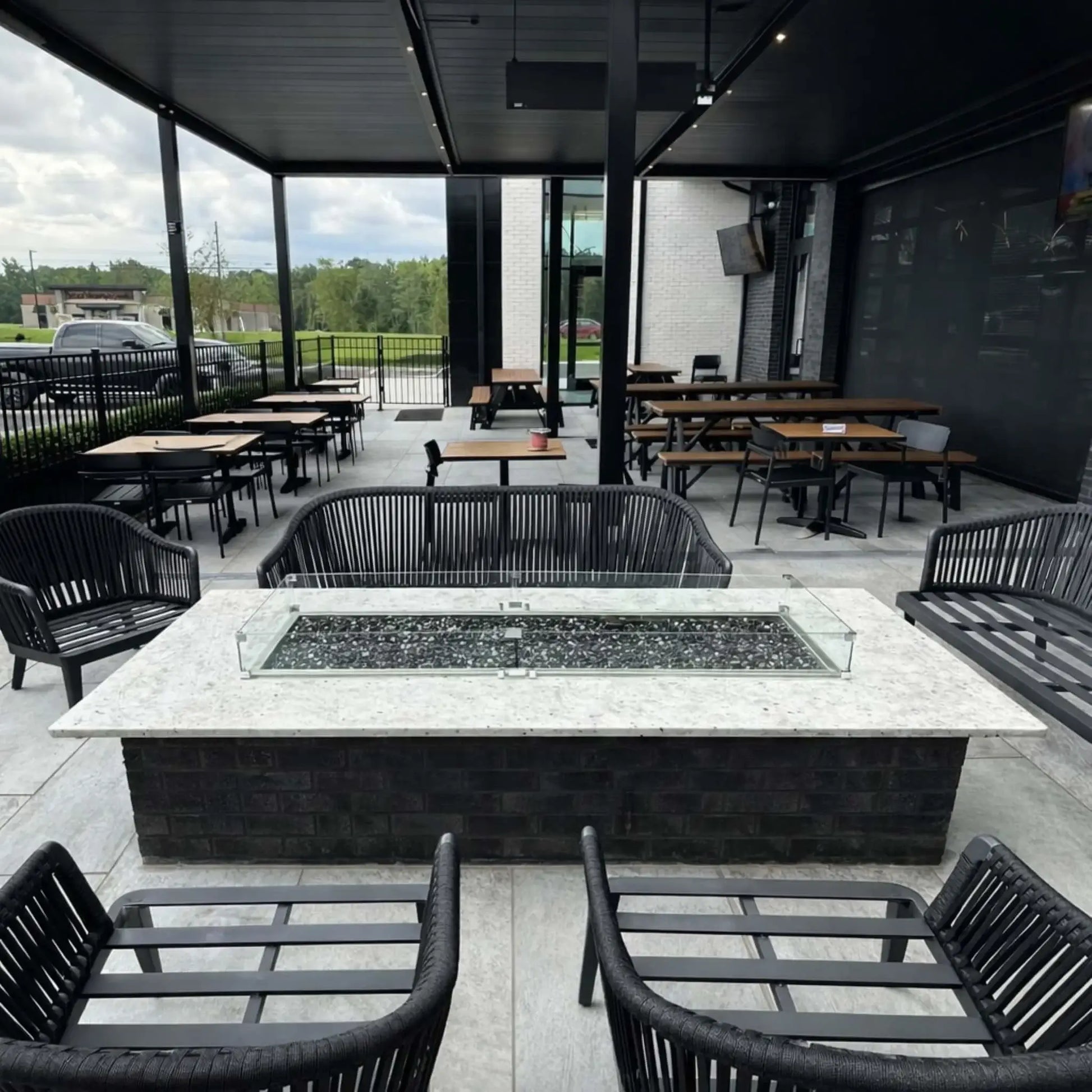Rooftop-style outdoor patio with city skyline at sunset, showcasing a rectangular fire table with Hearth Products Controls HPC Fire Rectangle Drop-In Pan H Burner Torpedo FPPK Push Button Flame Sensing FLEX system, surrounded by seating and overlooking urban high-rise buildings.