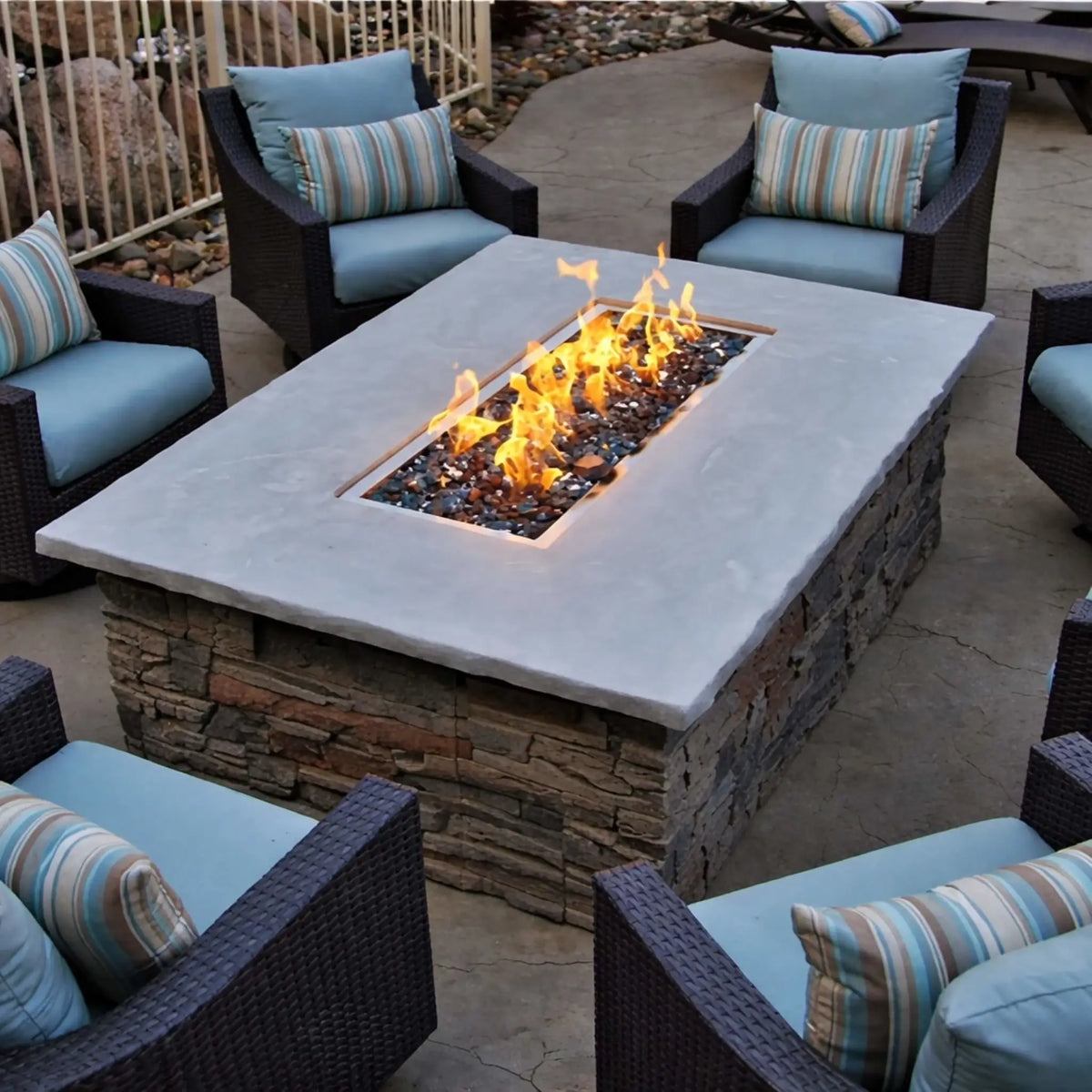 Square stone fire pit table showcasing HPC Fire Rectangle Drop-In Pan H Burner Torpedo Match Lit (CSA MLFPK Flex) with black fire glass, surrounded by cushioned outdoor chairs in a circular patio layout, highlighting a clean, modern backyard design.