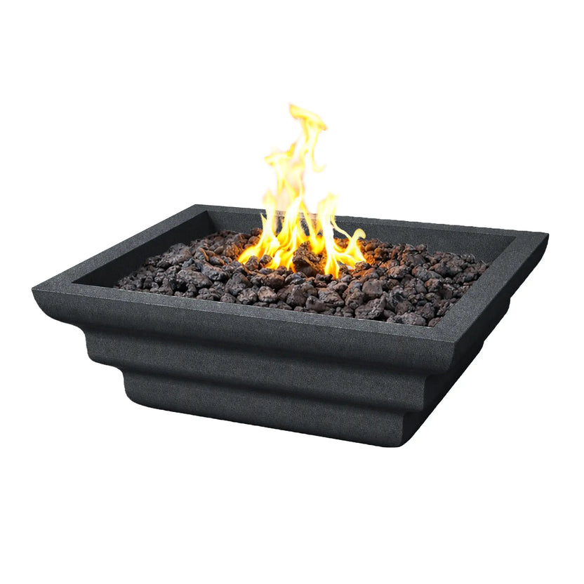Angled studio image of a black Shadow Cast Ripple Designer Series fire bowl by Flame Havens. The square fire bowl features sculpted ripple-style sides and a recessed burner area filled with dark lava rock. Bright yellow flames rise from the center, highlighting the textured finish and modern architectural design of the outdoor gas fire feature.