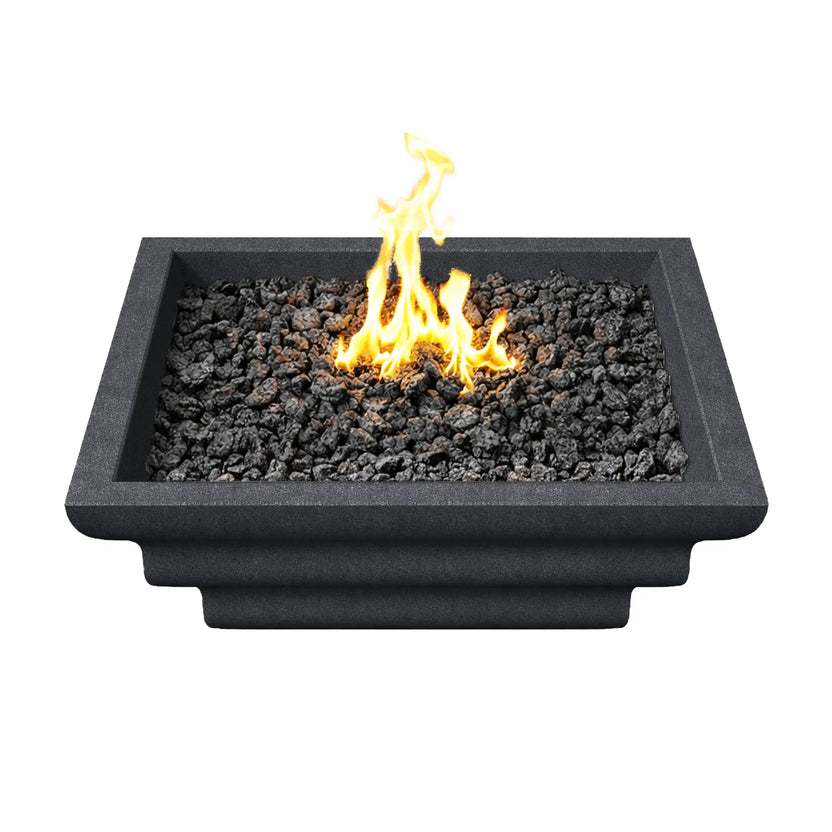 Top-down view of the black Shadow Cast Ripple Designer Series fire bowl filled with black lava rock media. A bright yellow gas flame rises from the center of the burner, surrounded by evenly distributed fire rock. The square architectural fire bowl features a thick rim and modern geometric profile designed for outdoor patios and poolside fire features.