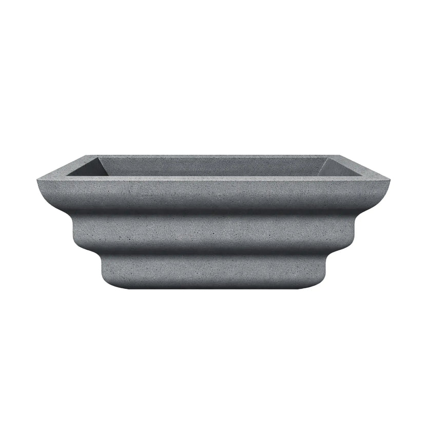 Side profile of the gray Shadow Cast Ripple Designer Series fire bowl with no burner or media installed. The sculpted ripple-style exterior creates three layered curves along the base, giving the bowl a distinctive architectural look. The square top opening and textured gray finish emphasize its modern outdoor fire feature design.