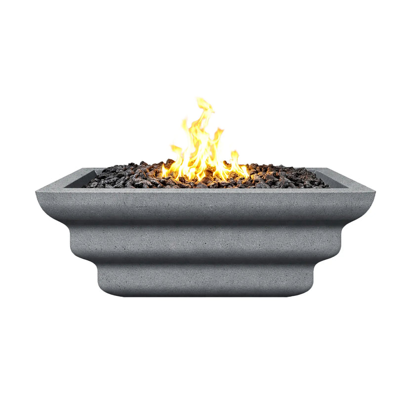Side view of the gray Shadow Cast Ripple Designer Series fire bowl burning with a bright yellow gas flame above black lava rock media. The bowl’s ripple-style sculpted sides and square rim are visible, while the textured gray concrete-like finish gives the fire feature a modern architectural appearance suitable for outdoor patios and landscape installations.
