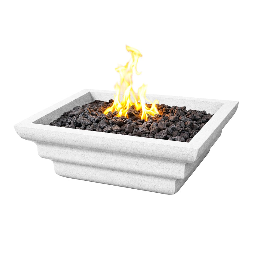 Angled product view of the white Shadow Cast Ripple Designer Series square fire bowl filled with black lava rock and an active gas flame rising from the center. The bowl features a textured white concrete-style finish with layered ripple sculpting along the sides, creating a modern outdoor fire feature designed for patios, pool areas, and landscape fire installations.